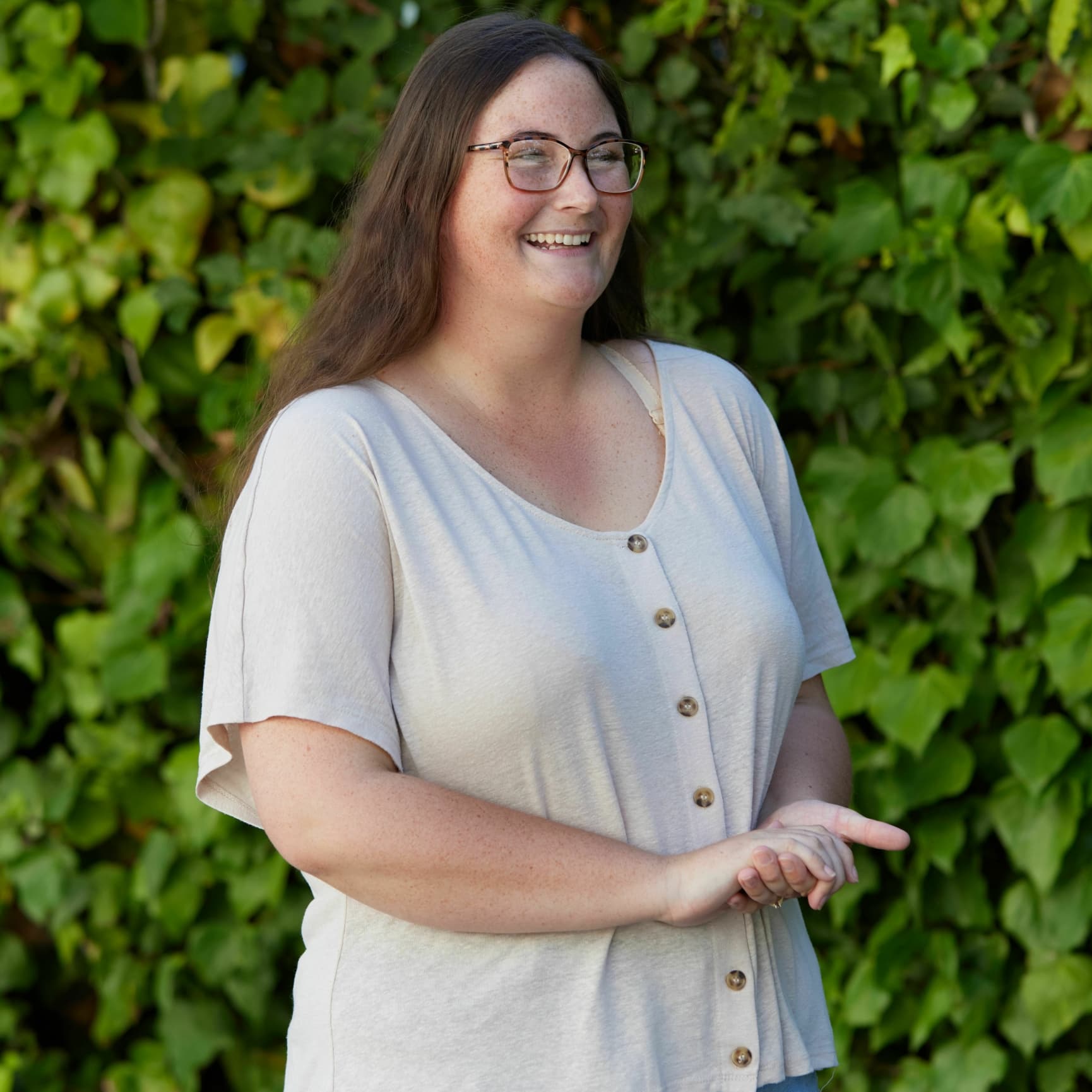 A young woman standing outside and smiling to the right of the camera