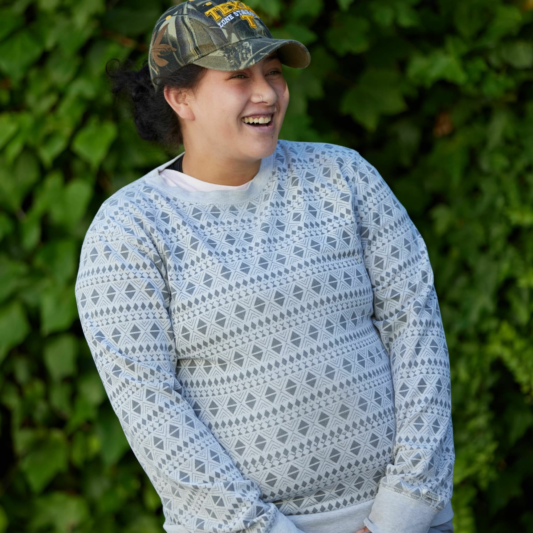 A picture of a young woman in a cap standing outside with her hands in her pockets and smiling to the right