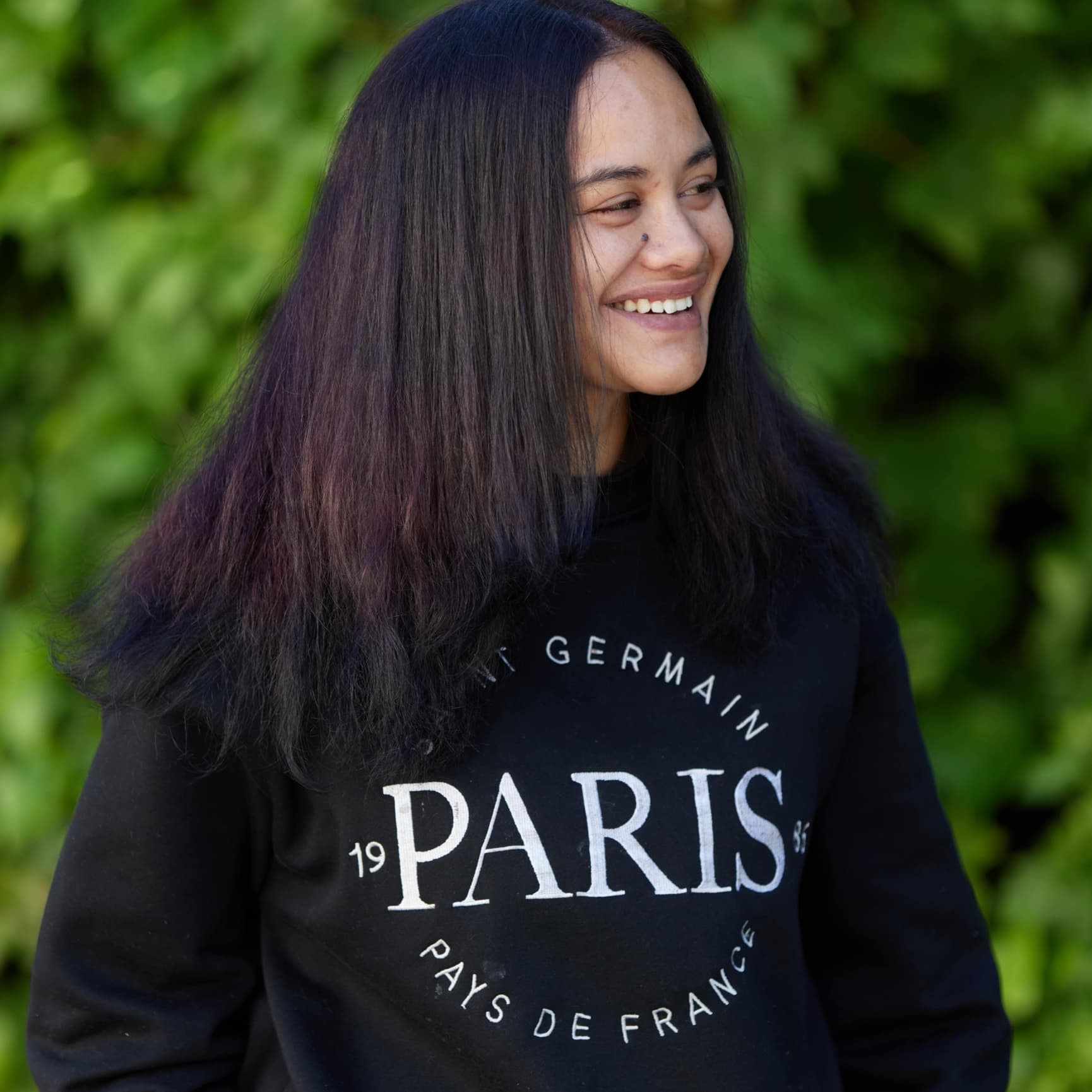 A young woman standing outside and smiling to the left